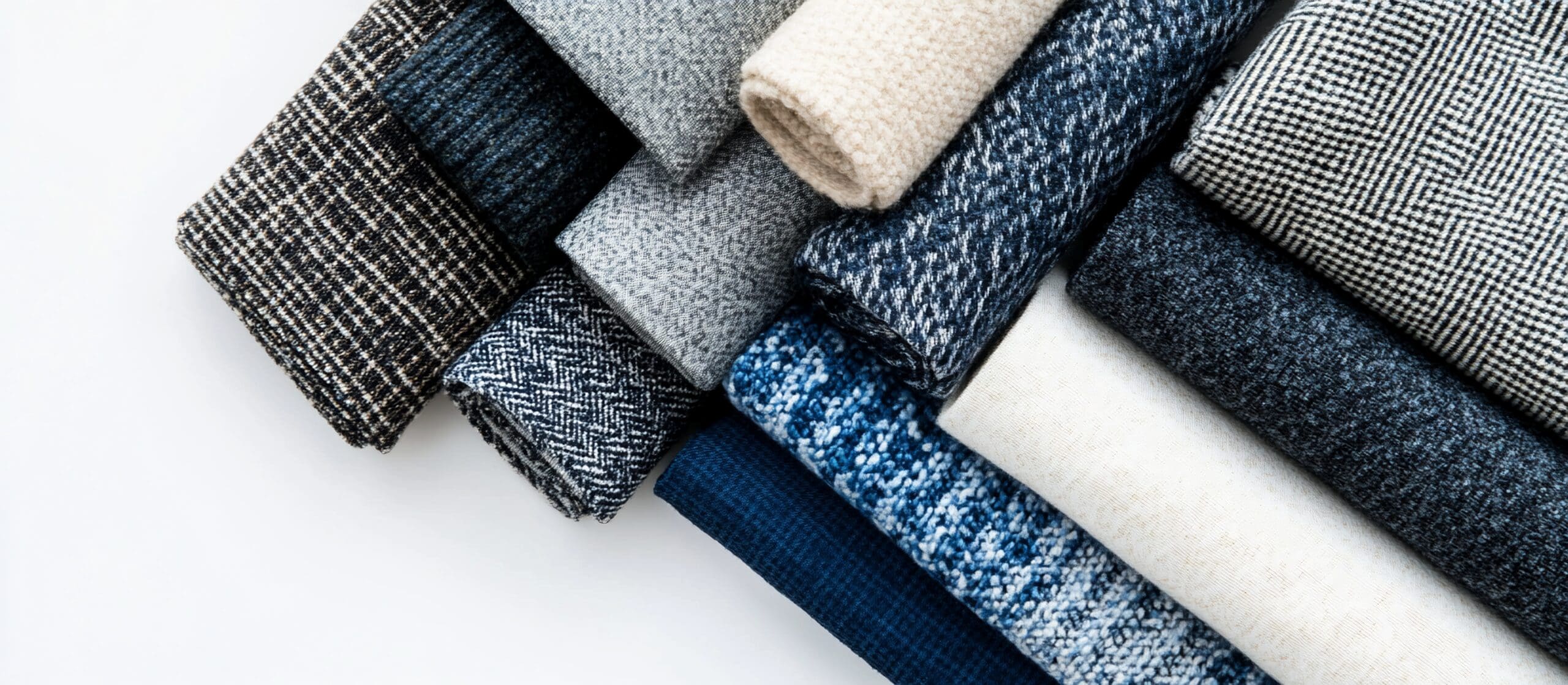 Rolled bolts of various blue, gray, and beige fabrics.